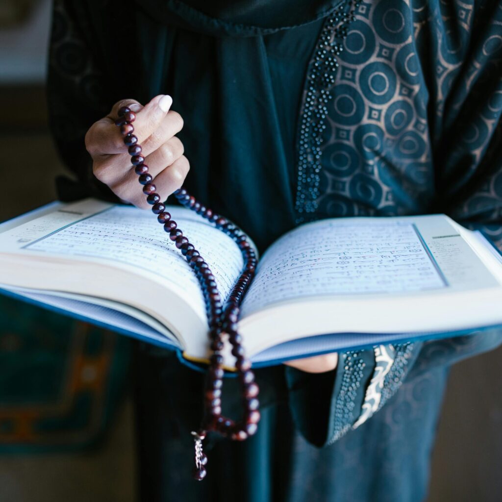 A woman in traditional attire reads a holy book with prayer beads, symbolizing faith and devotion.